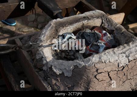 Un fabbro crea il braciere con braci con grandi tenaglie di carbone. Brace bagliore in una fucina di ferro. Fuoco, calore, carbone e cenere Foto Stock