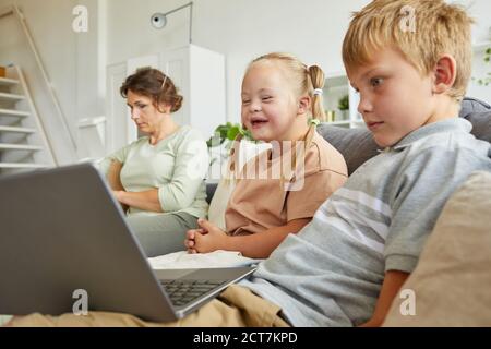 Ritratto di ragazza felice con la sindrome giù ridendo felice mentre guardando lo schermo del computer portatile e sedendosi sul divano con la famiglia a casa Foto Stock