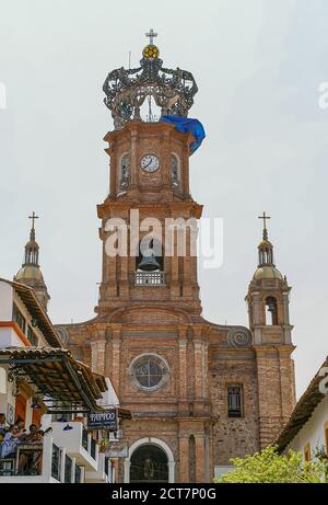 Puerto Vallarta, Messico - 25 aprile 2008: Chiesa di nostra Signora di Guadalupe . Closeup di mattoni marrone-rosso torre orologio in pietra contro cielo azzurro. Verde Foto Stock