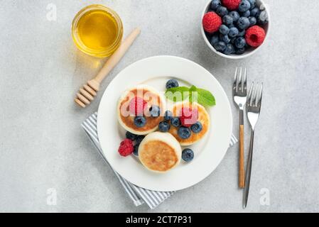 Frittelle di formaggio di cottage con frutti di bosco e miele serviti su un piastra Foto Stock