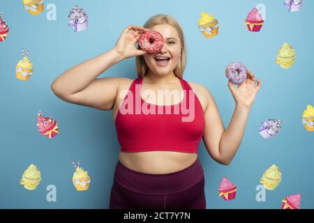 La donna grassa mangia dolce invece di fare palestra. Sfondo ciano Foto Stock