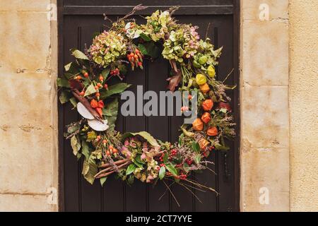 Corona con le bacche rosse e le foglie secche appese su una porta. Foto Stock