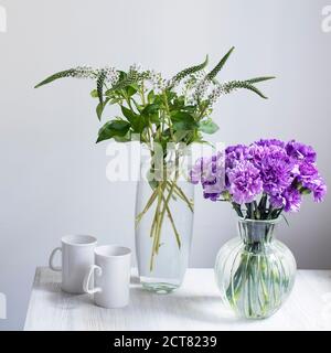 Bouquet nuziale di garofani lilla in quattro vasi rotondi di vetro di diverse dimensioni come decorazione della tavola. Due tazze bianche. Foto Stock