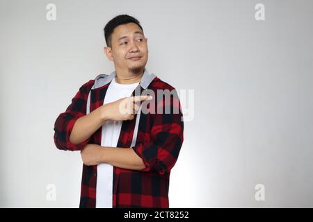 Ritratto di divertente giovane asiatico sorridente e puntando dietro di lui a presentare qualcosa, su sfondo grigio con copia spazio Foto Stock