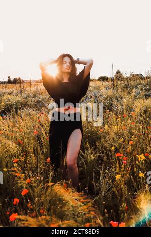 Ritratto estivo della natura della donna sottile bruna in nero lungo vestitevi con un papavero in posa su un prato di fiori selvatici Foto Stock