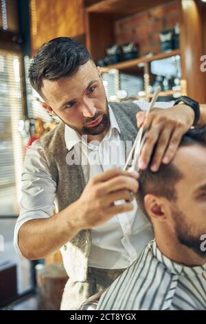 Stylist creativo che osserva messo a fuoco mentre dà un taglio dei capelli Foto Stock