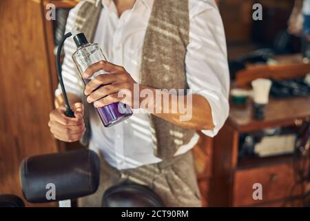 Stylist professionale per capelli che tiene una bottiglia spray al barbershop Foto Stock