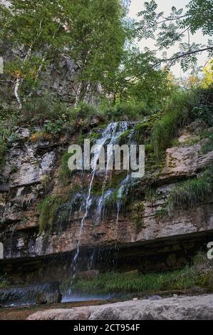 vista di una piccola cascata del fiume di montagna tra grandi ciottoli da una scogliera. Foto Stock