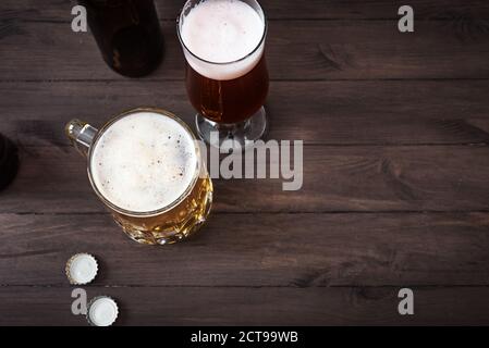 Vari tipi di birra alla spina in vetro e tazza su tavolo di legno, vista dall'alto, spazio per la copia. Birra fresca. Foto Stock