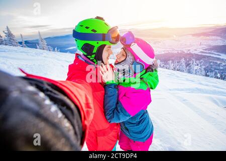 Selfie foto amante coppia snowboarder e sciatore tenendo le mani sullo sfondo delle montagne in inverno, luce solare. Stazione sciistica Concept Foto Stock