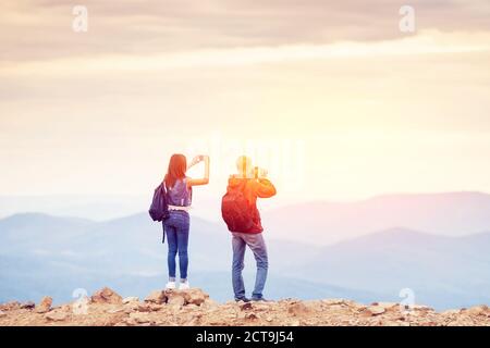 I viaggiatori felici, uomo e ragazza, conquistarono la cima della montagna, sollevano le mani con la fotocamera e scattano foto di paesaggi durante il viaggio Foto Stock