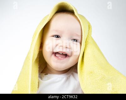 Foto di un bambino di undici mesi sorridente sotto un asciugamano giallo Foto Stock