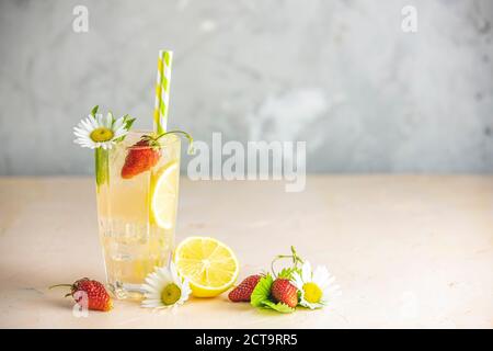 Bicchieri di bevanda rinfrescante ghiacciata con limone e fragola serviti su un tavolo rosa chiaro. Cocktail freschi con frutta ghiacciata, erbe e camomilla de Foto Stock