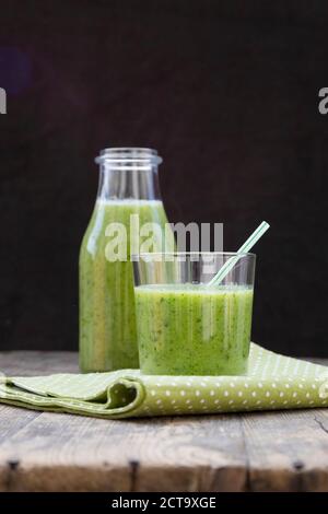 Bottiglia di vetro e il vetro del frullato verde, fatta di spinaci, insalata di rucola, mela, arancio, banana e cetriolo, sul tavolo di legno Foto Stock