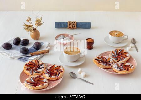 Piccole crostate di prugne su piatto con cannella e zucchero a velo su tavola di legno bianco, delizioso dessert sfoglia. Foto Stock