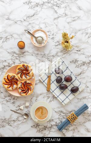 Piccole crostate di prugne su piatto con cannella e zucchero a velo su tavola di legno bianco, delizioso dessert sfoglia. Foto Stock