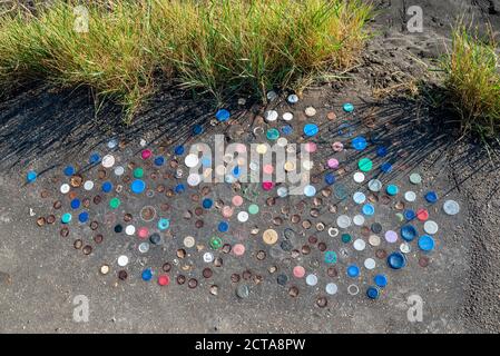 Le parti superiori delle bottiglie di plastica sono spinte nello strato di catrame del muro di mare a Chalkwell, Southend on Sea, Essex, UK. Cinder percorso sull'estuario del Tamigi con tappi per bottiglia Foto Stock