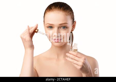 Donna Redhaired che applica l'olio cosmetico sul viso che posa in studio Foto Stock