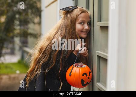 Vista laterale ritratto di mischievoius adolescente ragazza che ascolta alla porta mentre si gioca nascondere e cercare o trick o trattare sopra Halloween Foto Stock