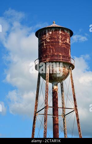 Una torre d'acqua arrugginita con vernice a pealing contro un cielo parzialmente nuvoloso. Foto Stock