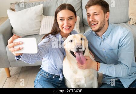 Giovane coppia che prende selfie con il loro cane a casa Foto Stock