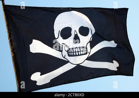 Jolly Roger scull e crossbones bandiera pirata battenti su un immagine fotografica blu trasparente Foto Stock