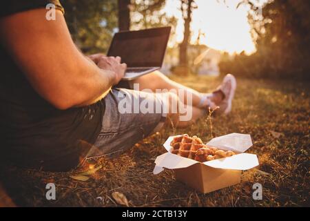 Waffle freschi vicino a Guy con computer portatile a terra, pasto americano da take-away. Foto Stock