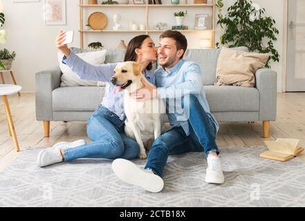 Giovane coppia che prende selfie con il loro cane in soggiorno Foto Stock