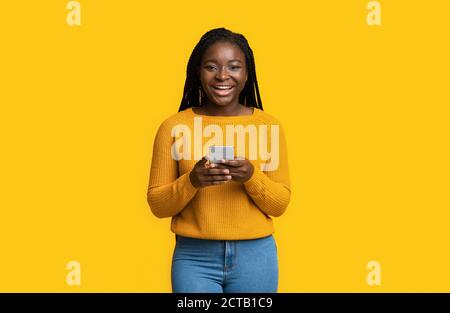 App. Cool. Allegro African Female Holding smartphone e sorridente a Camera Foto Stock