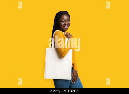 Donna Africana sorridente con borsa in tela di Tote vuota in tessuto Sfondo giallo Foto Stock