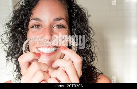 giovane donna sorridente che forma il cuore con i suoi allineatori invisibili in silicone per la correzione dentale. Trattamento dentale. Ortodonzia mobile. Foto Stock