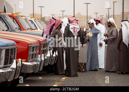 Un gruppo di uomini Kuwaiti vestiti in dishas godendo di una tazza di caffè arabico speziato con cardamomo quando espongono i loro camion vintage GMC. Foto Stock