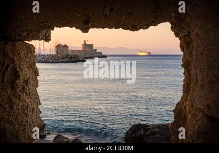 Vista incorniciata del tramonto sulla Fortezza di San Nicola e sui mulini a vento del porto di Mandraki, la città di Rodi, l'isola di Rodi, la Grecia Foto Stock