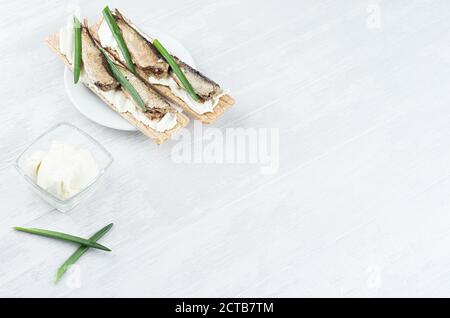 Fresco estivo salutare antipasto di pane intero grattugiato con conserve di spratti, cipolla verde, crema di formaggio su tavola di legno bianco, vista dall'alto, spazio copia Foto Stock