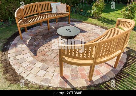 Due panche di legno con schienale rotondo su una bella pietra cerchio nel giardino Foto Stock