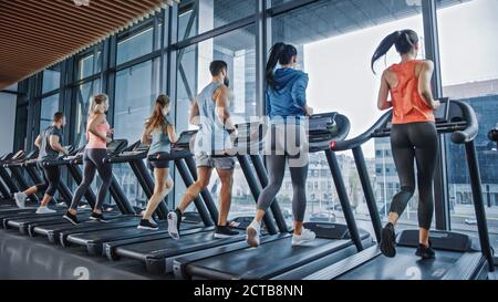 Gruppo di persone atletiche che corrono su tapis roulant, facendo esercizio di fitness. Atletica e muscolare Donne e uomini attivamente allenarsi nella palestra moderna Foto Stock