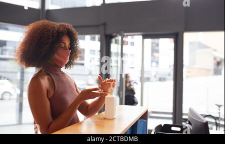 Misto razza Businesswoman in maschera viso utilizza disinfettante mani in Ricevimento in ufficio durante la Pandemia della Salute Foto Stock