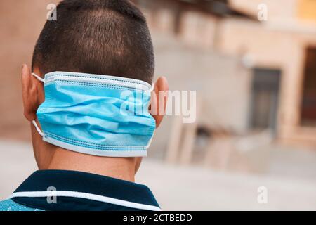 primo piano di un giovane uomo per strada, in abbigliamento casual, indossando la sua maschera monouso sul retro del collo mentre non lo indossa in faccia Foto Stock
