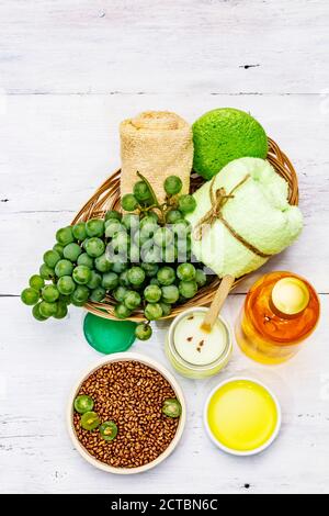 Accessori termali naturali e uva verde. Ingredienti freschi per una cura di sé sana e confortevole. Pannelli di legno bianco sfondo, vista dall'alto Foto Stock