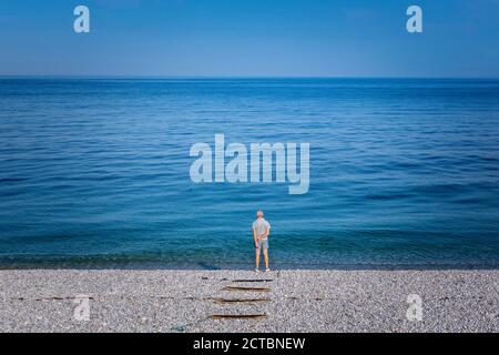 Uomo solitario sulla spiaggia che guarda all'orizzonte Foto Stock