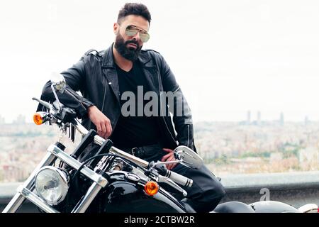 l'uomo vestito in pelle e indossando occhiali da sole pone accanto alla sua moto, concetto di libertà e stile di vita motociclista, spazio di copia per il testo Foto Stock