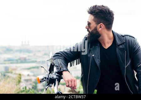 ritratto di un uomo bearded in una giacca di pelle appoggiata al manubrio della sua moto, concetto di libertà e stile di vita biker, spazio di copia per Foto Stock