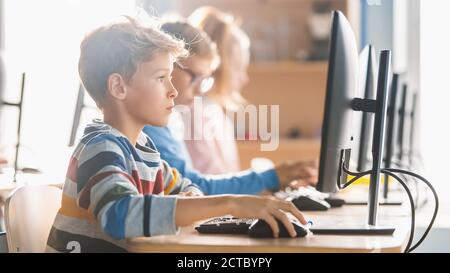 Scuola elementare Scienza Aula: Piccoli studenti intelligenti seduti in fila e lavorare su Personal computer, imparare linguaggio di programmazione per Foto Stock