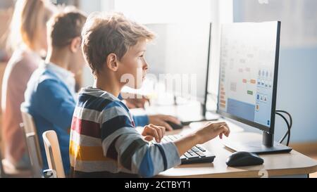 Scuola elementare Scienza Aula: Piccoli studenti intelligenti seduti in fila e lavorare su Personal computer, imparare linguaggio di programmazione per Foto Stock