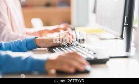 Primo piano in School computer Science Classroom: Piccoli studenti intelligenti che lavorano Personal computer, digitando su tastiere, utilizzando il mouse del computer Foto Stock