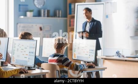 Scuola elementare Informatica Classroom: L'insegnante usa il Tablet computer, spiega la lezione a diversi gruppi di bambini intelligenti. Classe informatica - Bambini Foto Stock