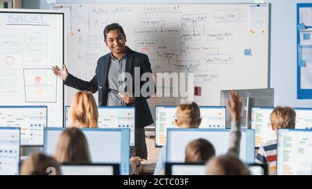 Classe Scuola elementare: L'insegnante utilizza la lavagna interattiva digitale, spiega la lezione a un gruppo diversificato di bambini intelligenti. I bambini stanno diventando moderni Foto Stock