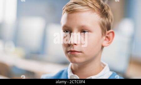 Ritratto di un piccolo ragazzo serio e concentrato seduto al suo banco della scuola. Piccolo ragazzo intelligente con il viso serio seduto in aula. Primo piano Foto Stock