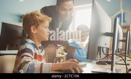 Scuola elementare di scienze aula: Un insegnante entusiasta parla con uno studente intelligente. Utilizzo di Personal computer per imparare il linguaggio di programmazione e. Foto Stock