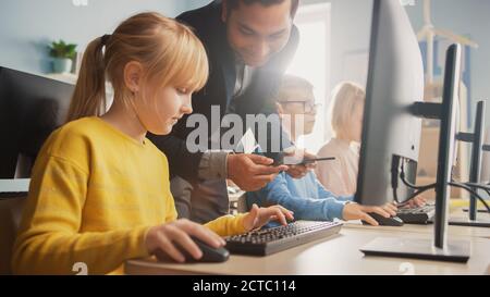 Scuola elementare Scienza aula: Insegnante spiega a una piccola scuola intelligente come usare Personal computer, per imparare linguaggio di programmazione necessario Foto Stock